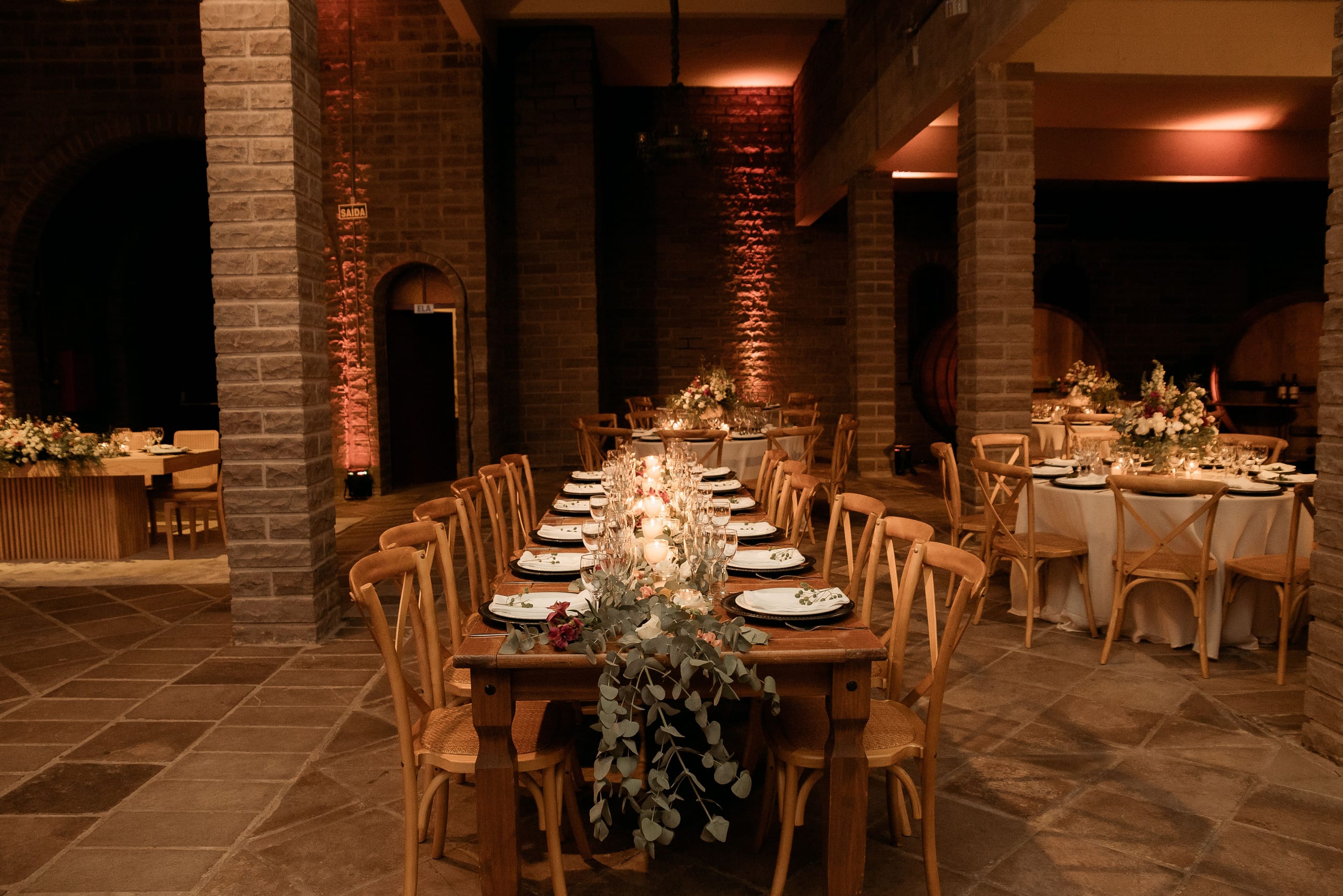 A warm brick hall with a long candlelit table set and waiting for the evening's guests