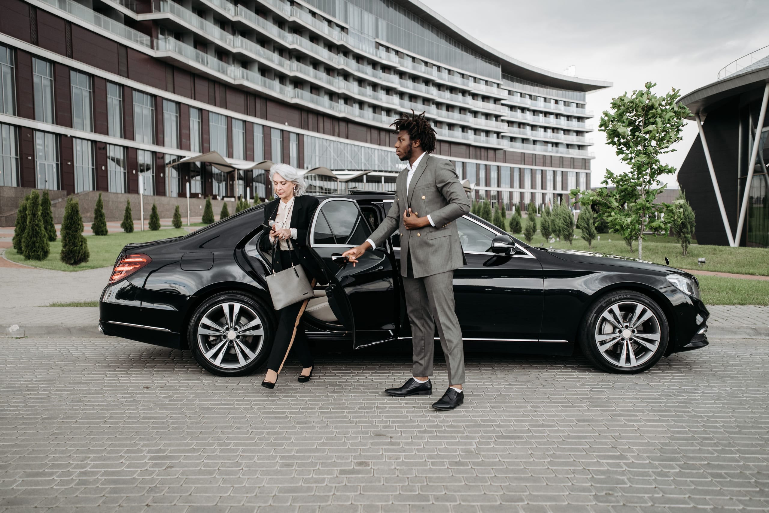 A chauffeur holds the door of a black car as a guest steps out, arriving for the evening