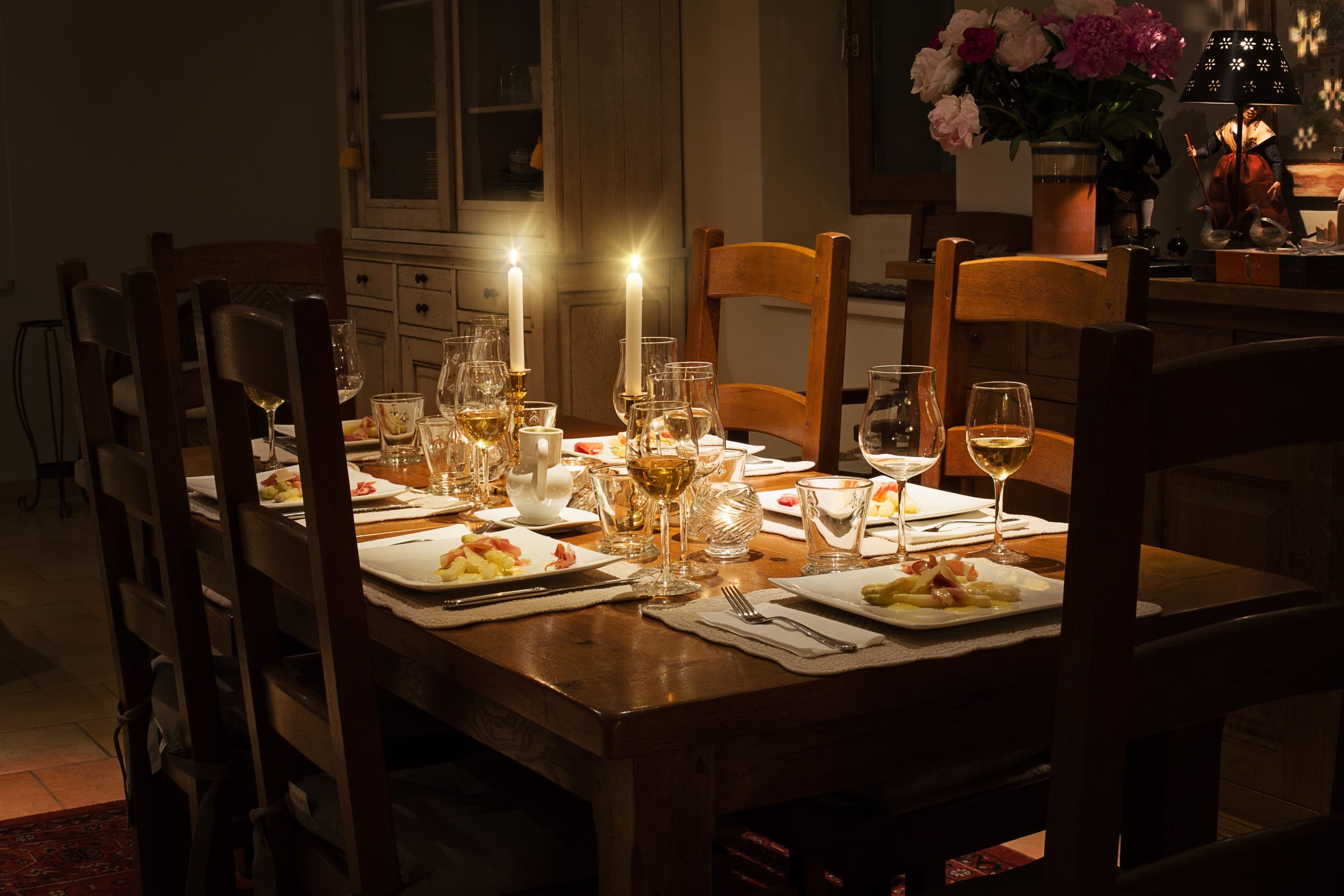 A candlelit table in a private house, laid with care for a small dinner among friends