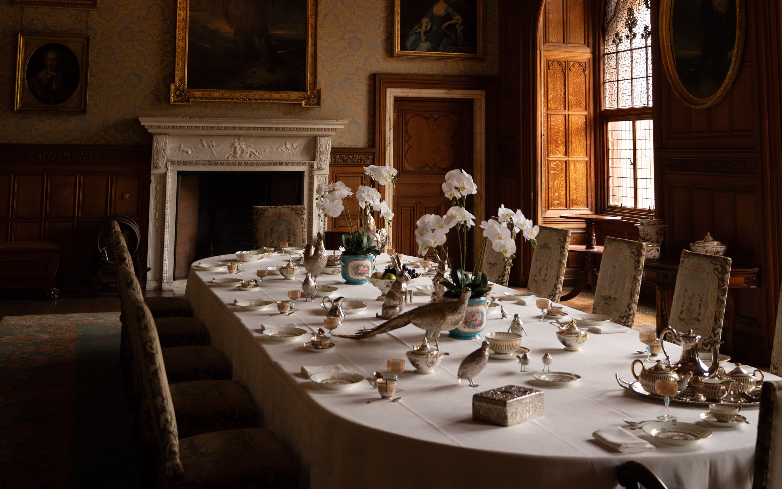 A quiet panelled dining room hung with portraits, its long table laid with white orchids and silver before the guests arrive